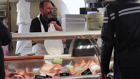 Butcher-at-food-market-in-Antibes,-France,-interacting-with-customers-over-meat-counter