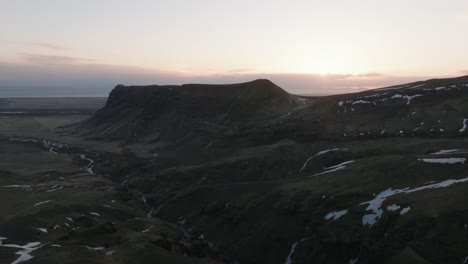 Aerial-panoramic-view-of-sunrise-sunlight-shining-over-green-mountain-peaks,-in-Iceland