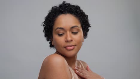 beauty-and-people-concept--portrait-of-happy-smiling-young-african-american-woman-with-bare-shoulders-touching-her-face-over-grey-background