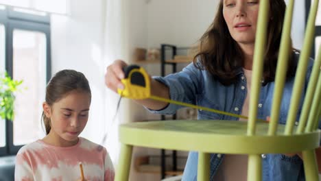 Concepto-De-Familia,-Bricolaje-Y-Mejoras-Para-El-Hogar-Feliz-Madre-Sonriente-E-Hija-Con-Regla-Midiendo-Una-Vieja-Silla-De-Madera-Para-La-Renovación-En-Casa