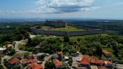 Drone-aerial-landscape-pan-over-local-town-with-housing-and-Chlemoutsi-medieval-Castle-fortress-Museum-on-hill-mountaintop-Clermont-Greece-Europe-archaeology