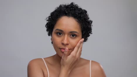 beauty-and-people-concept--portrait-of-happy-smiling-young-african-american-woman-with-bare-shoulders-touching-her-face-over-grey-background