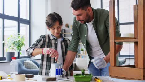 Concepto-De-Reparación,-Bricolaje-Y-Mejoras-Para-El-Hogar-Padre-E-Hijo-Con-Guantes-Protectores-Revolviendo-Pintura-De-Color-Gris-En-Lata-Para-Pintar-Una-Vieja-Mesa-De-Madera-En-Casa