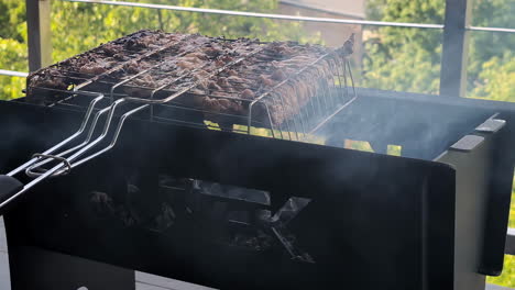 Still-shot-of-hot-charcoal-smoking-with-metal-utensils-slow-cooker-roasting-meat-chicken-poultry-pork-on-grill-outdoor-barbecue-BBQ-on-balcony-patio-heat-outdoors