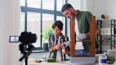 Concepto-De-Renovación,-Bricolaje-Y-Blogs-Padre-E-Hijo-Con-Guantes-Pegando-Cinta-Adhesiva-A-Una-Vieja-Mesa-De-Madera-Para-Repintar-Y-Grabar-Videos-Tutoriales-En-Casa