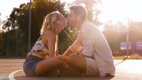 Vacaciones-De-Verano,-Tecnología-Y-Concepto-De-Personas-Pareja-Feliz-Con-Teléfonos-Inteligentes-Y-Auriculares-Escuchando-Música-Y-Besándose-Al-Aire-Libre