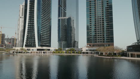 Genießen-Sie-Einen-Weiten,-Nach-Oben-Gerichteten-Blick-Auf-Die-Jumeirah-Lake-Towers-Mit-Ruhigem-Wasser-Und-Palmenumgebung,-Die-Die-Beeindruckenden-Gebäude-Hervorheben