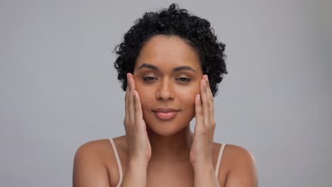 beauty-and-people-concept--portrait-of-happy-smiling-young-african-american-woman-with-bare-shoulders-touching-her-face-over-grey-background