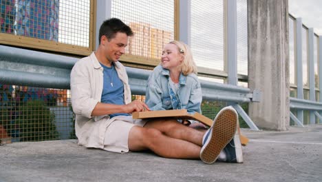 summer-holidays,-food-and-people-concept--happy-young-couple-eating-takeaway-pizza-on-city-street