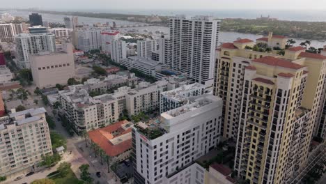 Drone-Volando-Sobre-West-Palm-Beach-Durante-El-Día,-Con-Tejados-Y-Edificios-Debajo-Y-Agua-En-El-Horizonte