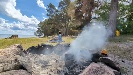 Woman-relax-near-Camping-pit-fire-extinguished,-steam-vapour-coming-out