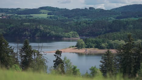 A-panorama-view-of-a-tranquil-Vltava-River-surrounded-by-lush-green-hills,-lush-meadows,-and-dense-forests,-offering-a-serene-natural-setting-in-a-parallax-video