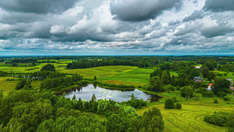 Cumulus-clouds-flowing-over-a-rural-countryside-reflecting-off-the-water-of-a-pond---aerial-hyper-lapse