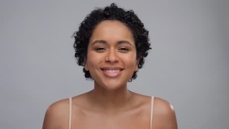 beauty-and-people-concept--portrait-of-happy-smiling-young-african-american-woman-with-bare-shoulders-blowing-to-flower-petals-over-grey-background