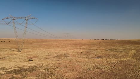 Expansive,-high-voltage-power-lines-stretching-across-rural-farmland-in-a-remote-countryside-landscape---captured-with-a-drone