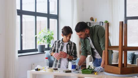 Concepto-De-Reparación,-Bricolaje-Y-Mejoras-Para-El-Hogar-Padre-E-Hijo-Con-Guantes-Protectores-Revolviendo-Pintura-De-Color-Gris-En-Lata-Para-Pintar-Una-Vieja-Mesa-De-Madera-En-Casa