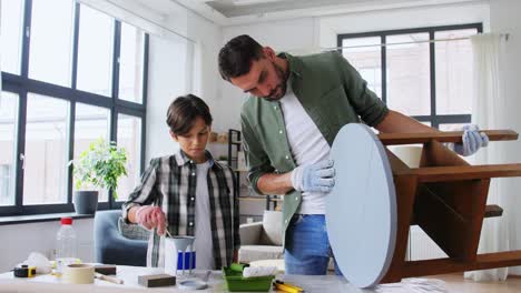 Concepto-De-Reparación,-Bricolaje-Y-Mejoras-Para-El-Hogar-Padre-E-Hijo-Con-Guantes-Protectores-Revolviendo-Pintura-De-Color-Gris-En-Lata-Para-Pintar-Una-Vieja-Mesa-De-Madera-En-Casa