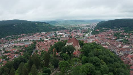 A-european-town-surrounded-by-hills-and-lush-greenery-under-a-cloudy-sky,-aerial-view