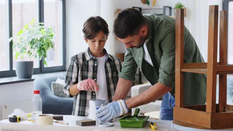 Concepto-De-Reparación,-Bricolaje-Y-Mejoras-Para-El-Hogar-Padre-E-Hijo-Con-Guantes-Protectores-Revolviendo-Pintura-De-Color-Gris-En-Lata-Para-Pintar-Una-Vieja-Mesa-De-Madera-En-Casa