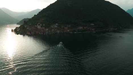 Boat-cruising-on-Lake-Iseo-in-Italy,-surrounded-by-mountains-and-a-quaint-lakeside-village