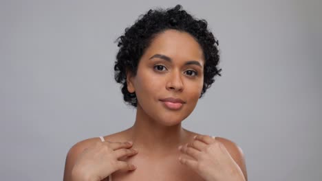 beauty-and-people-concept--portrait-of-happy-smiling-young-african-american-woman-with-bare-shoulders-touching-her-face-over-grey-background