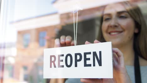 Kleines-Unternehmen,-Wiedereröffnung-Und-Service-Konzept-Glücklich-Lächelnde-Frau-Hängt-Wiedereröffnungsbanner-An-Fenster-Oder-Türglas