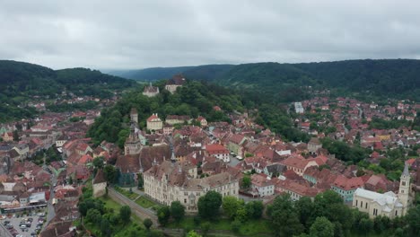 A-charming-european-town-nestled-in-lush-green-hills-on-a-cloudy-day,-aerial-view