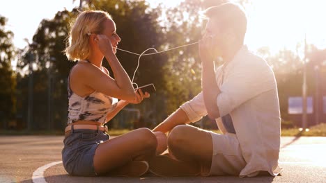 Vacaciones-De-Verano,-Tecnología-Y-Concepto-De-Personas-Pareja-Feliz-Con-Teléfonos-Inteligentes-Y-Auriculares-Escuchando-Música-Y-Besándose-Al-Aire-Libre