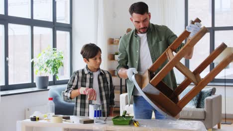 Concepto-De-Reparación,-Bricolaje-Y-Mejoras-Para-El-Hogar-Padre-E-Hijo-Con-Guantes-Protectores-Revolviendo-Pintura-De-Color-Gris-En-Lata-Para-Pintar-Una-Vieja-Mesa-De-Madera-En-Casa