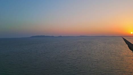 Aerial-drone-view-of-infinite-road-and-salt-water-lake-on-both-sides-in-Kutch,-Road-to-heaven-during-sunset-Gujarat,-India-4K