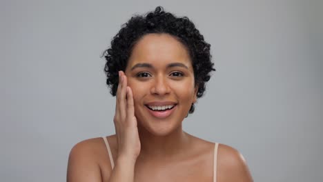 beauty-and-people-concept--portrait-of-happy-smiling-young-african-american-woman-with-bare-shoulders-touching-her-face-over-grey-background