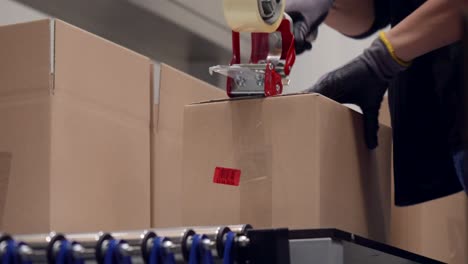 Worker-assembling-the-box-from-the-cardboard,-close-shot-of-a-labour-folding-the-board-into-a-carton-and-sticking-the-tape-to-seal-it