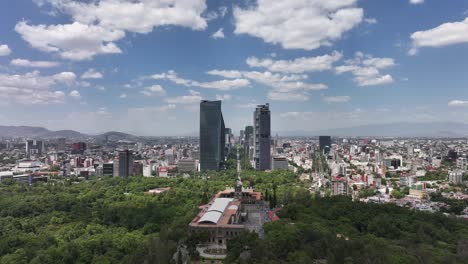 Daytime-descending-aerial-over-Chapultepec-Castle-and-park,-viewing-Chapultepec-Avenue-and-skyscrapers-in-Mexico-City