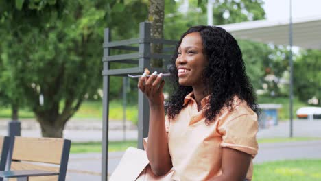 Concepto-De-Tecnología-Y-Personas-Feliz-Mujer-Afroamericana-Sonriente-Usando-Una-Grabadora-De-Comandos-De-Voz-En-Un-Teléfono-Inteligente-En-La-Ciudad