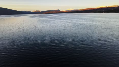 Drohnenaufnahme,-Die-Mit-Einem-Blick-Auf-Ruhiges-Wasser-Beginnt,-Das-Aufsteigt-Und-Die-Nordische-Landschaft-Mit-Den-Bergen-Offenbart