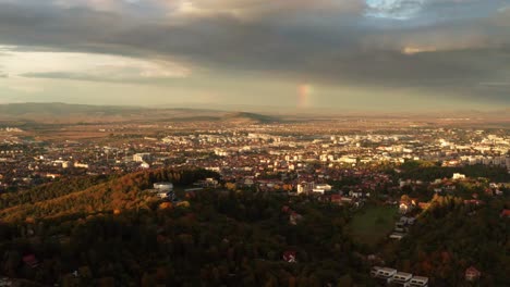 Vista-Aérea-Del-Atardecer-De-Una-Ciudad-Rodeada-De-Verdes-Colinas-Y-Un-Vasto-Paisaje.