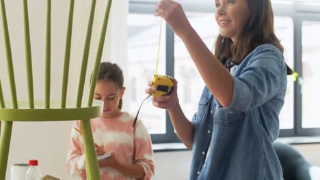 Familien-,-Heimwerken--Und-Heimwerkerkonzept,-Glücklich-Lächelnde-Mutter-Und-Tochter-Mit-Lineal,-Das-Einen-Alten-Holzstuhl-Für-Die-Renovierung-Zu-Hause-Misst