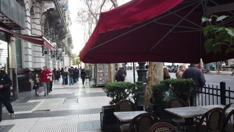 Red-umbrella-coffee-bar-situated-in-busy-downtown-avenue-at-heritage-architecture-of-Buenos-Aires-city,-a-postcard-of-European-Argentine-tradition