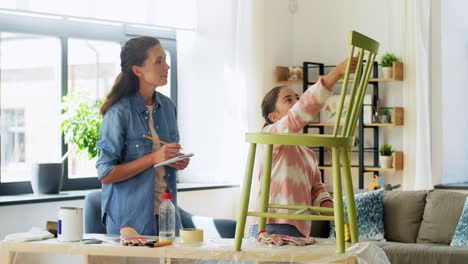 Concepto-De-Familia,-Bricolaje-Y-Mejoras-Para-El-Hogar-Feliz-Madre-Sonriente-E-Hija-Con-Regla-Midiendo-Una-Vieja-Silla-De-Madera-Para-La-Renovación-En-Casa