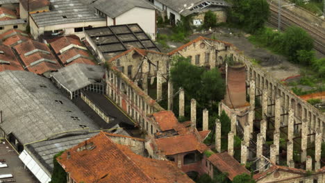 Abandoned-ceramic-factory-in-Italy,-showcasing-old-buildings-and-overgrown-greenery,-aerial-view