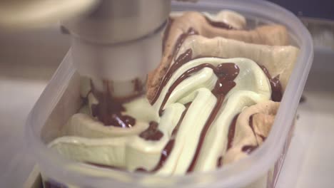 Close-shot-of-a-mechanical-arm-filling-the-freshly-made-ice-cream-in-a-pattern-in-squround-container