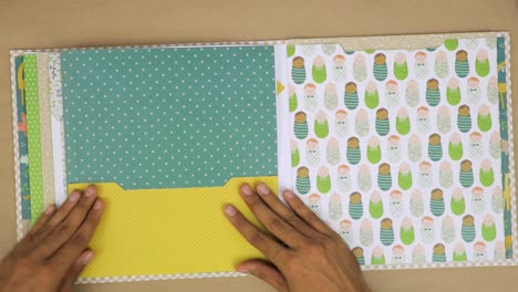 Hands-working-on-colorful-baby-themed-scrapbook-with-patterned-papers-and-decorative-elements