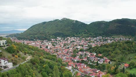 Un-Pintoresco-Pueblo-Enclavado-En-Exuberantes-Colinas-Verdes-En-Un-Día-Nublado,-Vista-Aérea