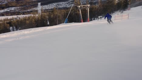 Male-skier-doing-big-carving-turns-on-a-nice-slope-with-low-sun-and-forest-in-the-background