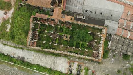 An-abandoned-ceramic-factory-in-italy-overgrown-with-greenery-and-decaying-structures,-aerial-view