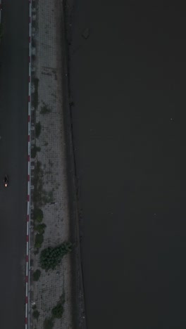 Top-down-aerial-view-tracking-motorbike-traffic-along-a-narrow-road-next-to-a-canal