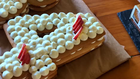 Close-up-of-pastry-chef-person's-hands-placing-strawberry-apple-fruit-onto-number-4-four-letter-cake-baking-birthday-celebrations-decorations-pavlova-icing