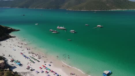 Aerial-drone-footage-of-Arraial-do-Cabo,-Cabo-Frio:-showcasing-stunning-blue-waters,-pristine-white-sandy-beaches,-and-majestic-island-mountains-with-a-leftward-panoramic-view