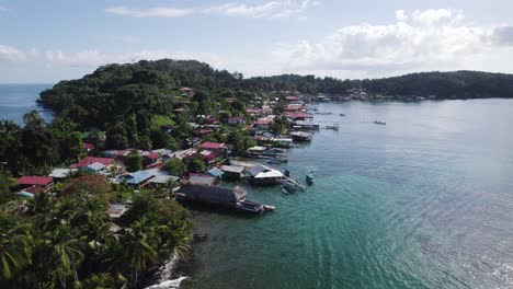 Aerial-view-of-serene-seaside-village-surrounded-by-lush-greenery-and-peaceful-waters,-showcasing-colorful-rooftops-and-scenic-landscapes-under-a-blue-sky