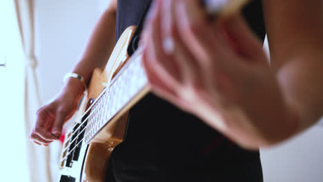 Beautiful-closed-slow-motion-shot-of-a-young-woman's-hands-and-fingers-playing-an-electric-bass-guitar-in-a-recording-studio-with-dim-entry-light-through-the-balcony